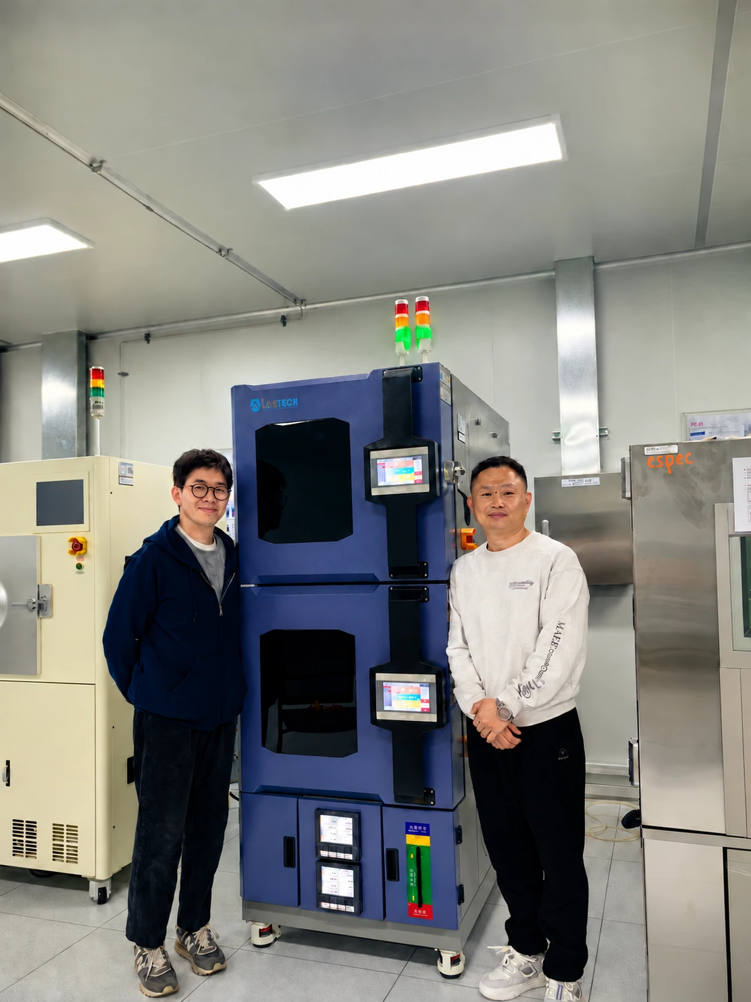 Two people beside a LABTECH-branded environmental test chamber in a laboratory
